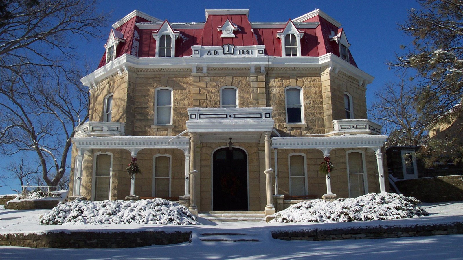 A three story stone house with steep red roof powdered in snow.