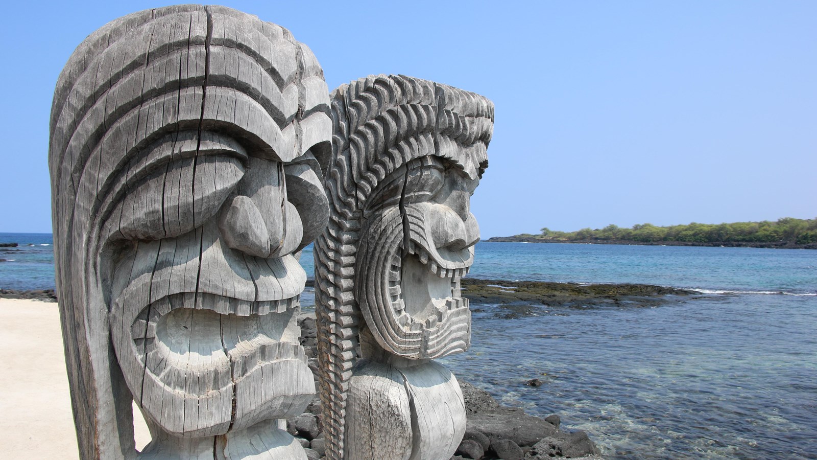 A pair of intricately carved kiʻi (temple images) stand facing the waters of Hōnaunau Bay