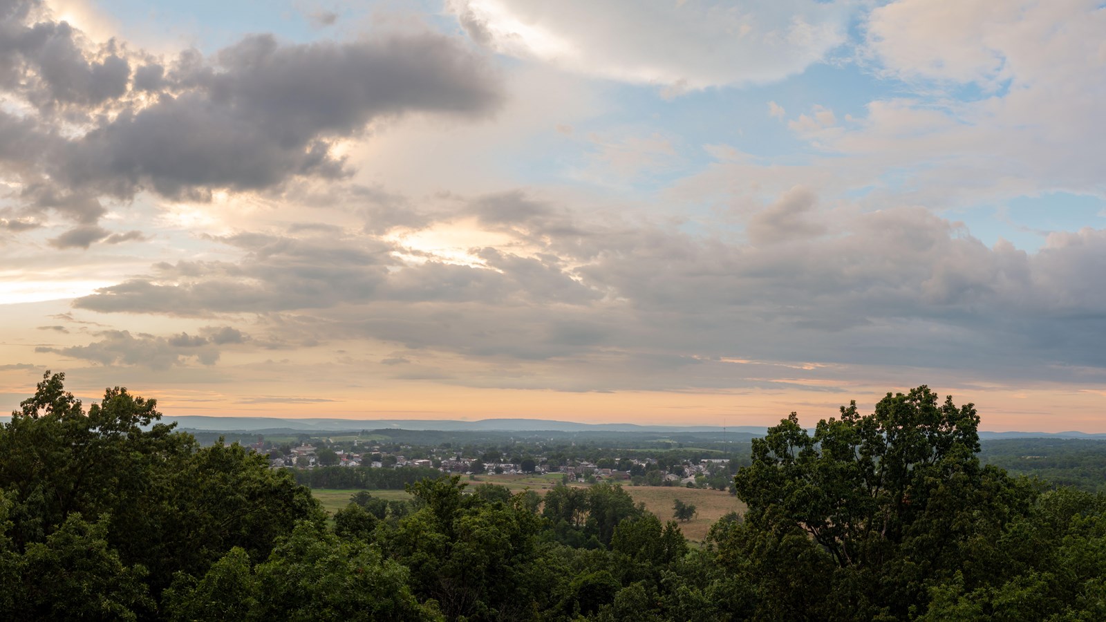 A view over lush trees to a small town in the distance with the sun setting.
