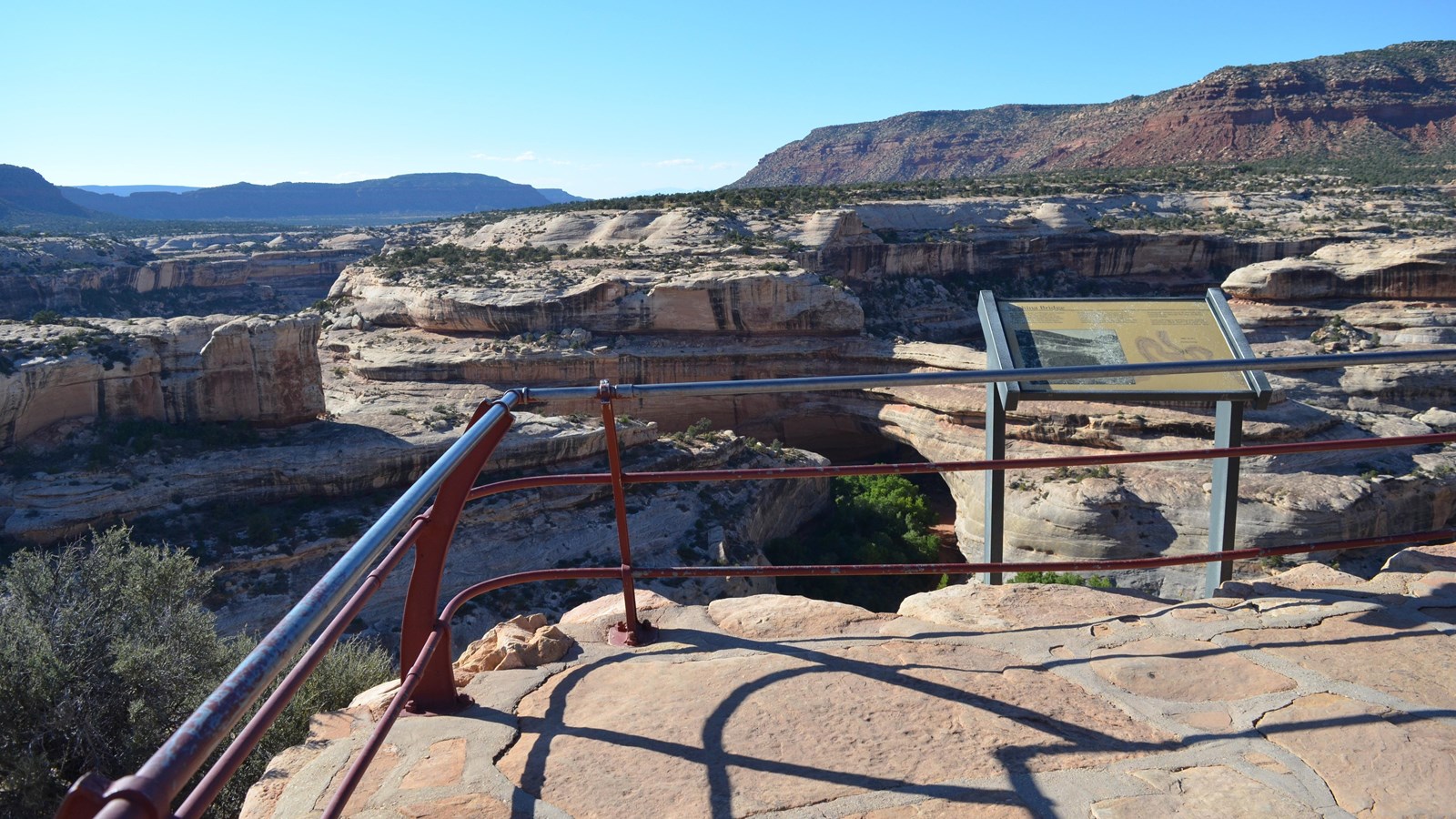 a viewing area with railing, Kachina Bridge in the canyon below