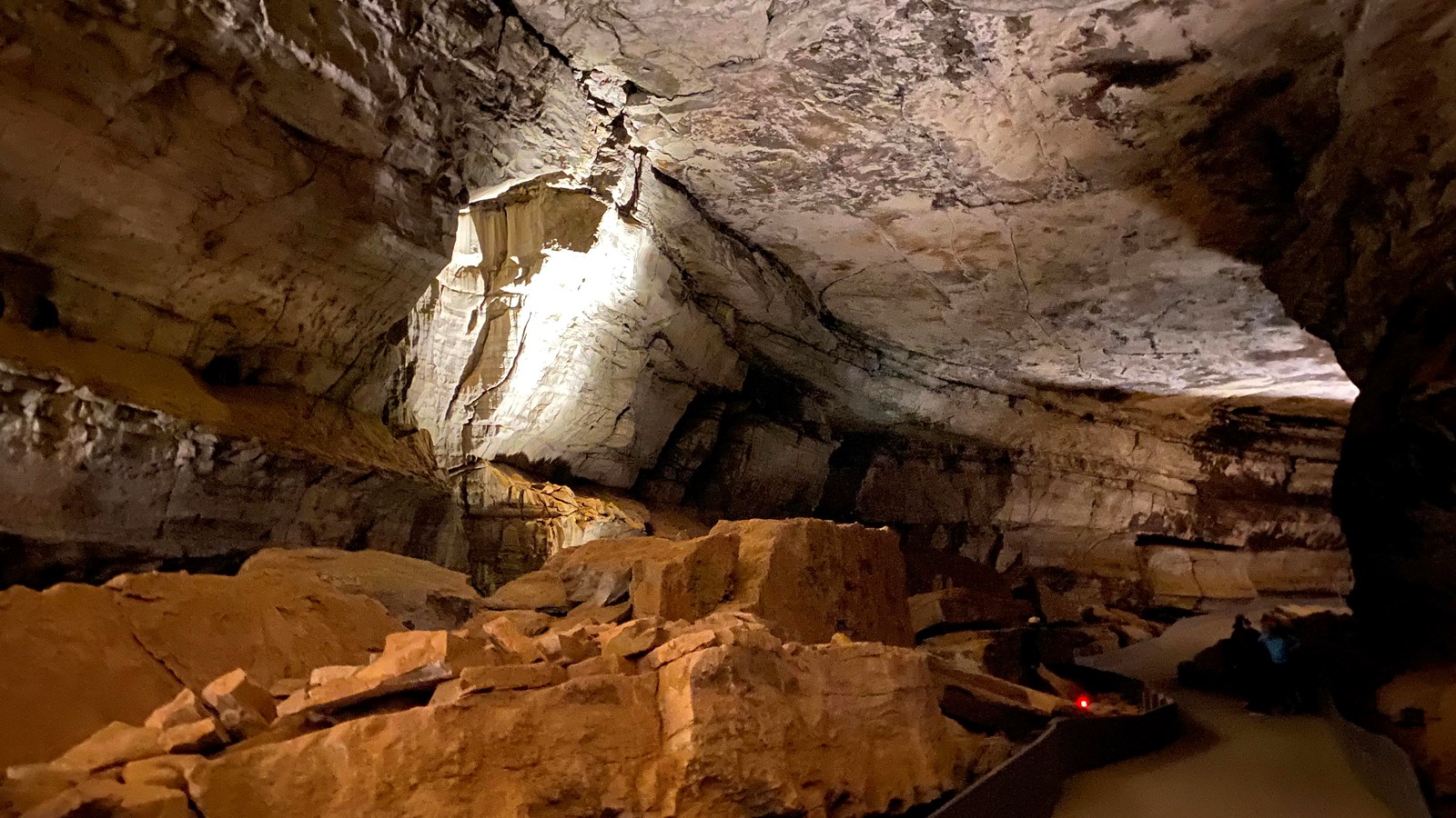 A paved trail on the right side of a cave passage with large rocks on the left side. 
