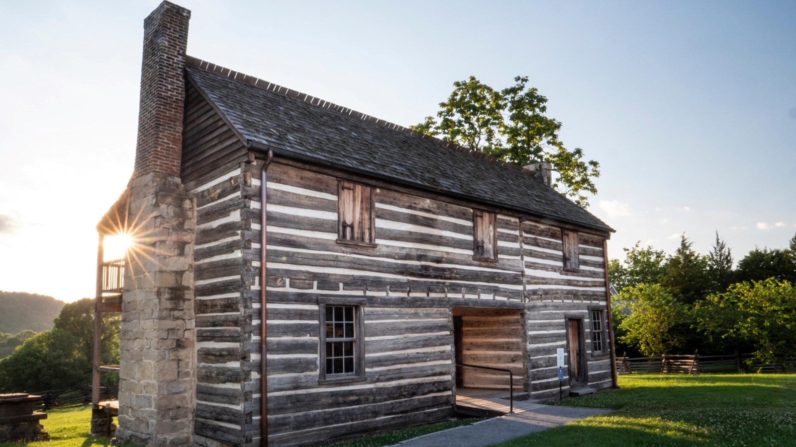 The sun shines behind a two-story log cabin.
