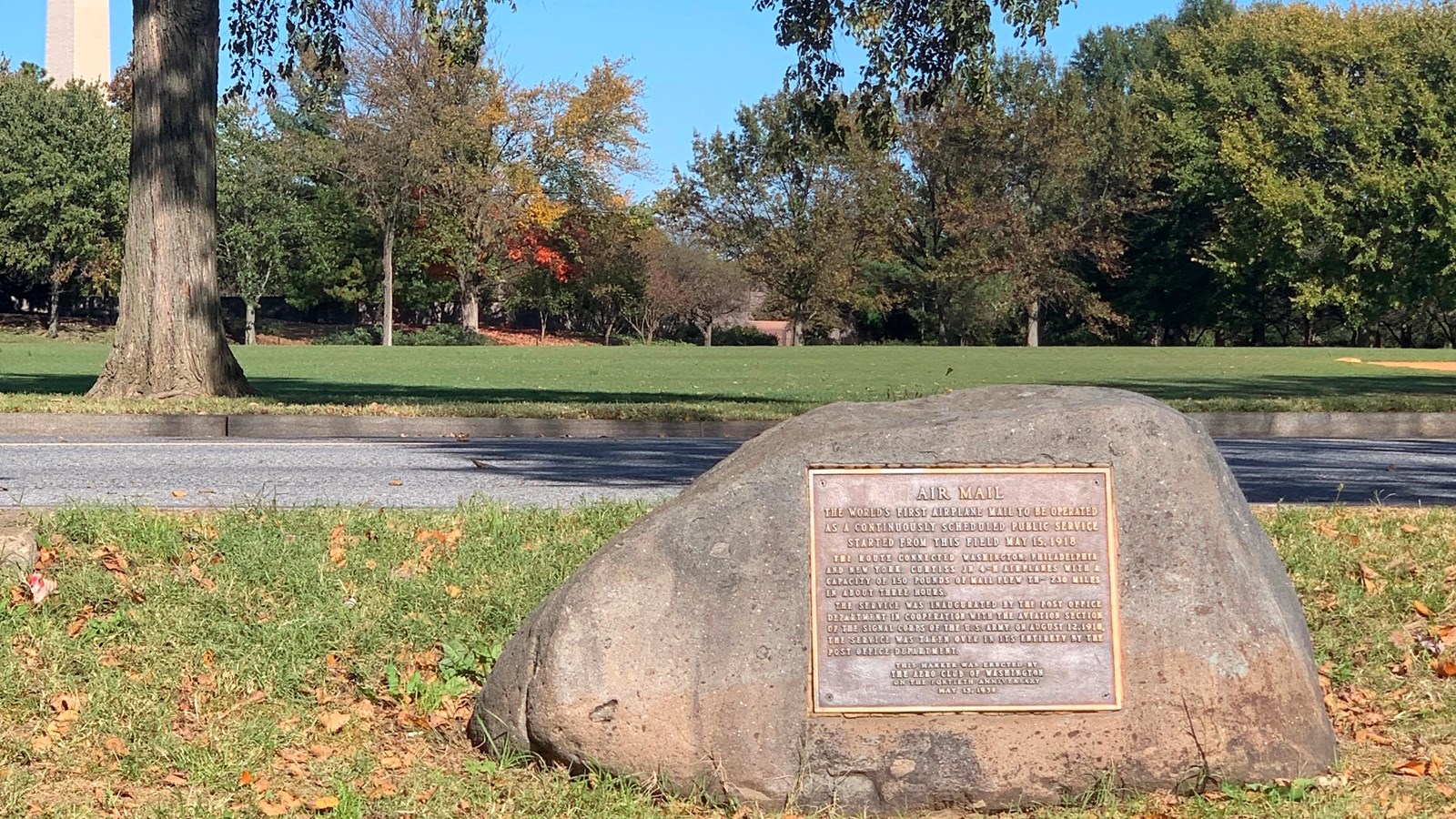 Large stone affixed with bronze plaque in a field, trees in the background
