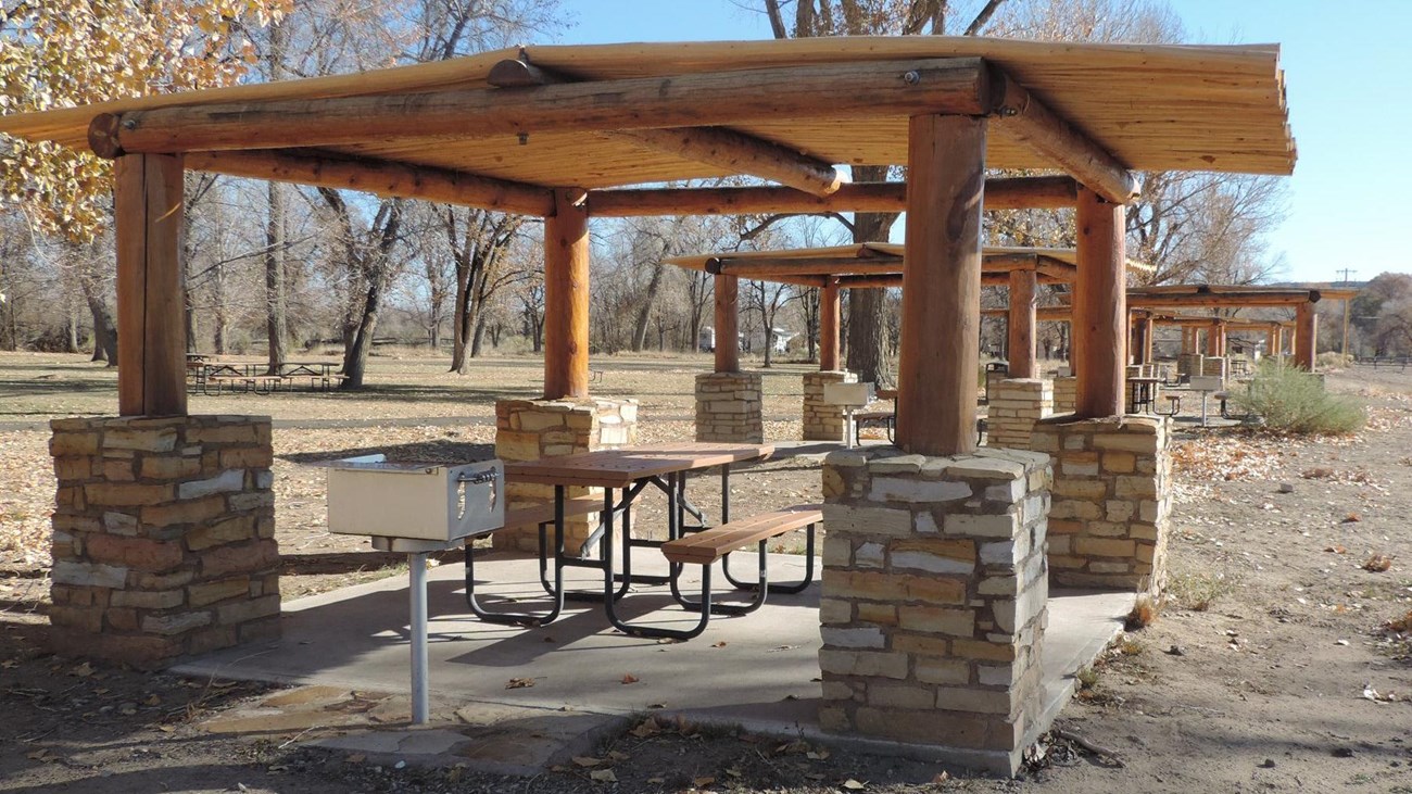 A photo of a picnic table under shade shelter next to a grill.