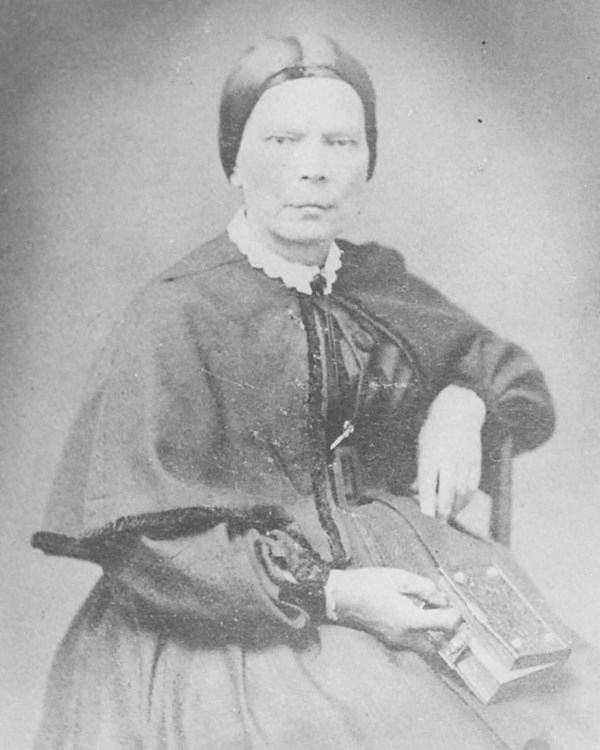 Black and white portrait of 19th century woman. She is sitting holding a book.