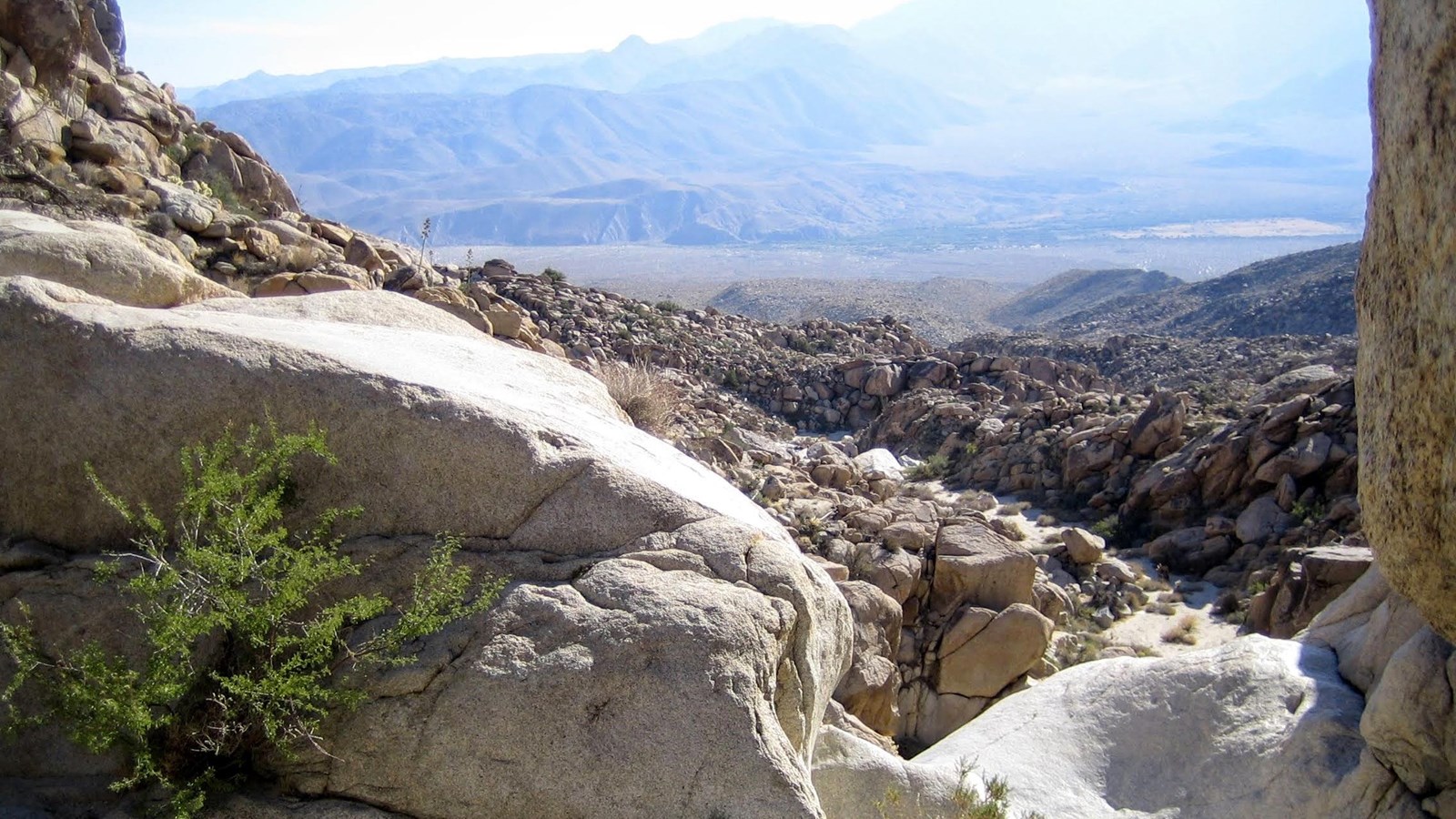 A view of a desert valley framed by exposed rock and boulders