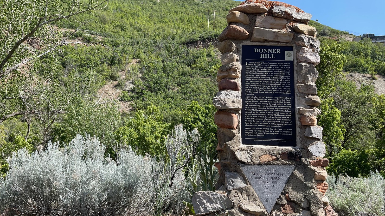 A Donner Hill stone monument stands amongst brush and grass hill.
