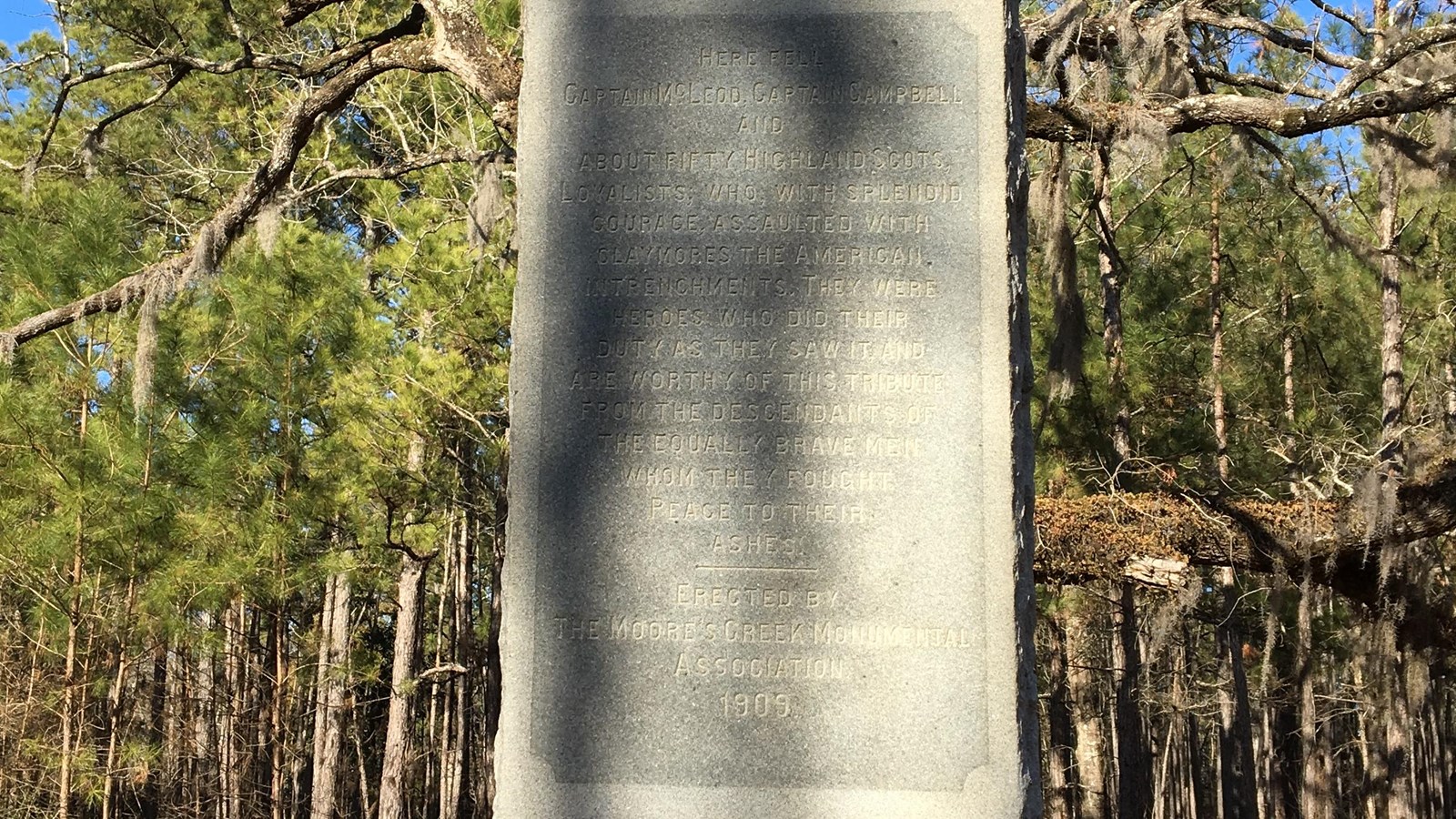 Granite Monument surrounde by trees alongside a black path.