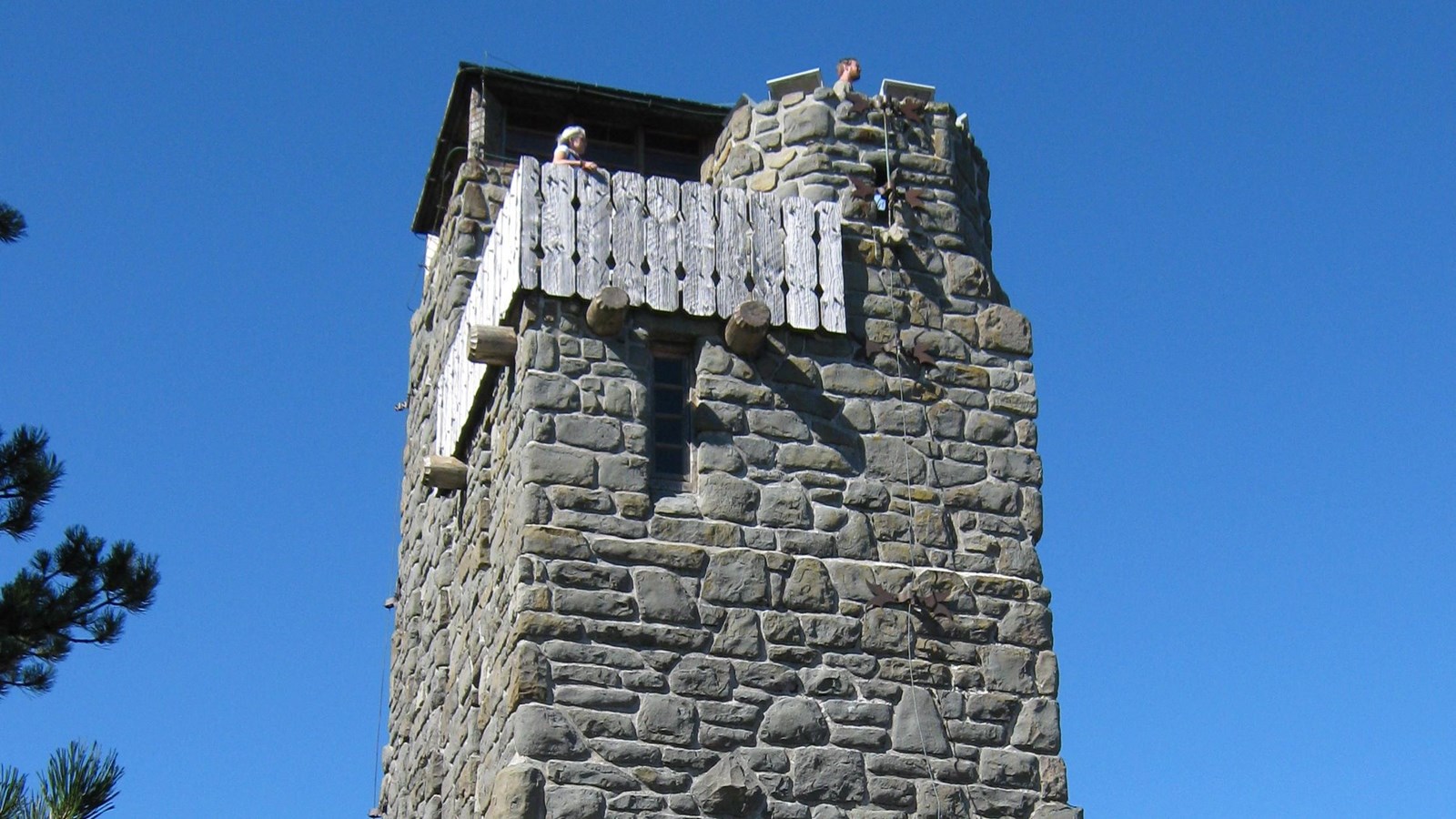 Color photograph of a stone tower with people in a cupola at the top on a clear day