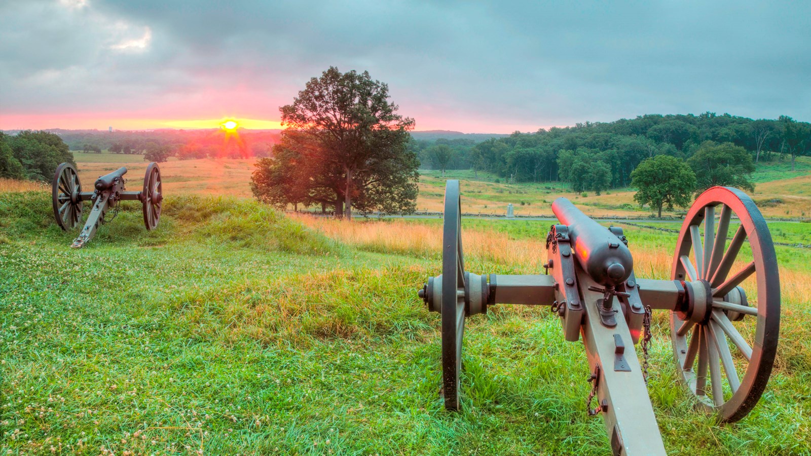 A pair of cannons overlooking an open field during sunset