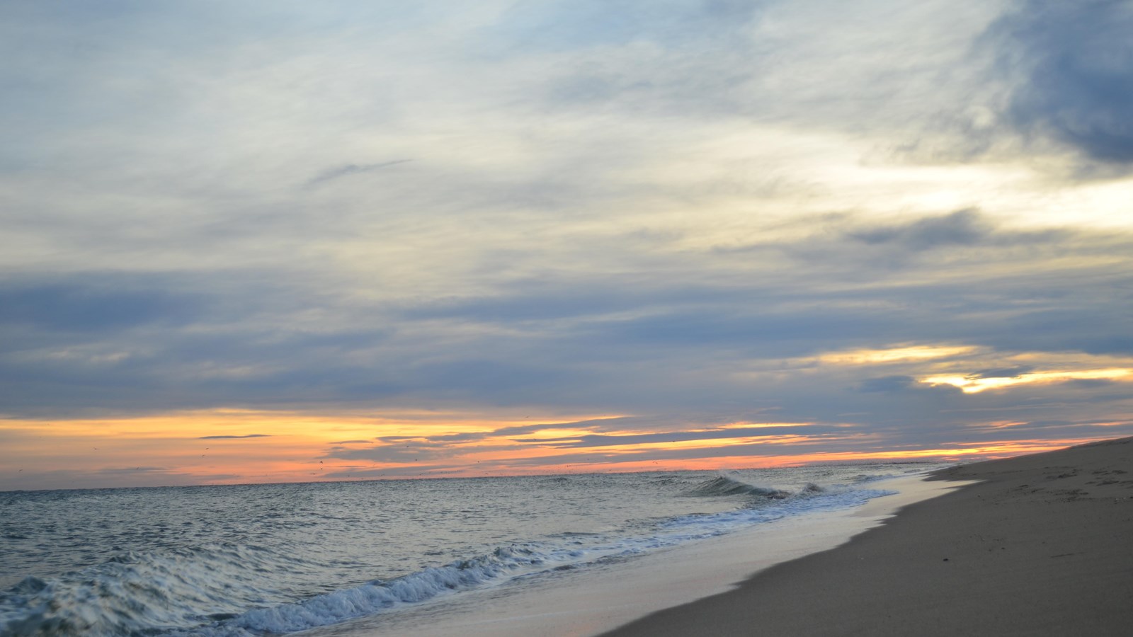 A streak of orange at the horizon is sandwiched between gray sky and ocean.