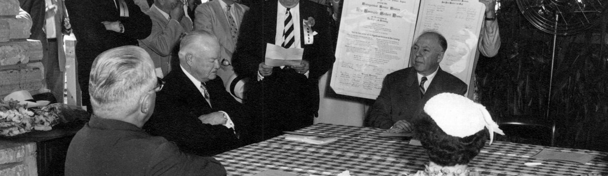 A 1950s photo depicts dignitaries honoring a distinguished old man at a picnic shelter.