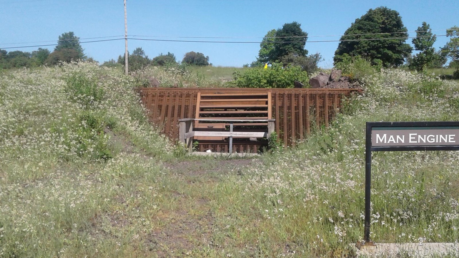 Rusted rail, pipes and fencing cover an old mining shaft that is surrounded by a grassy area.