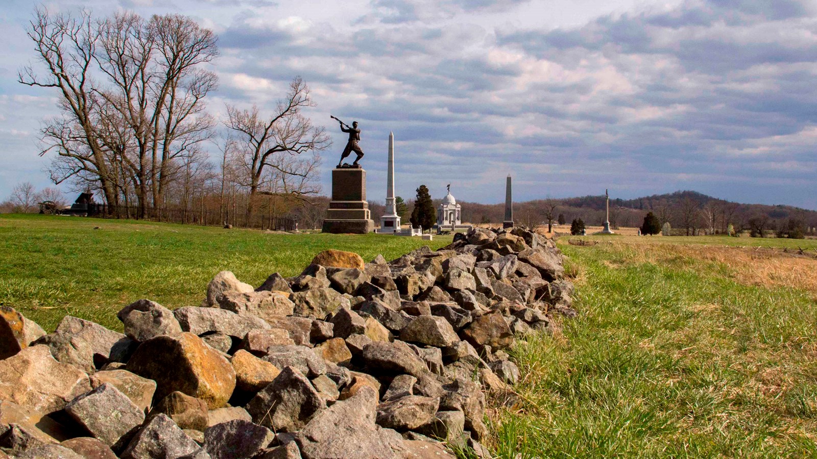 A stone wall with grass on either side. Monuments line the wall.