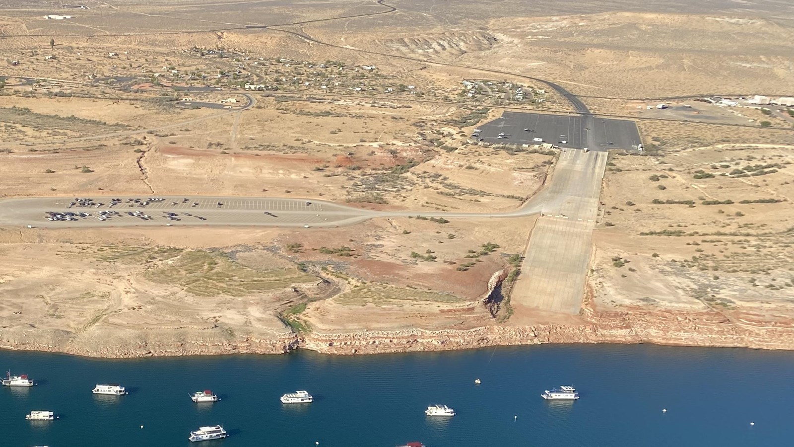 Aerial view of a concrete launch ramp that does not reach the water. Large parking lot to the left