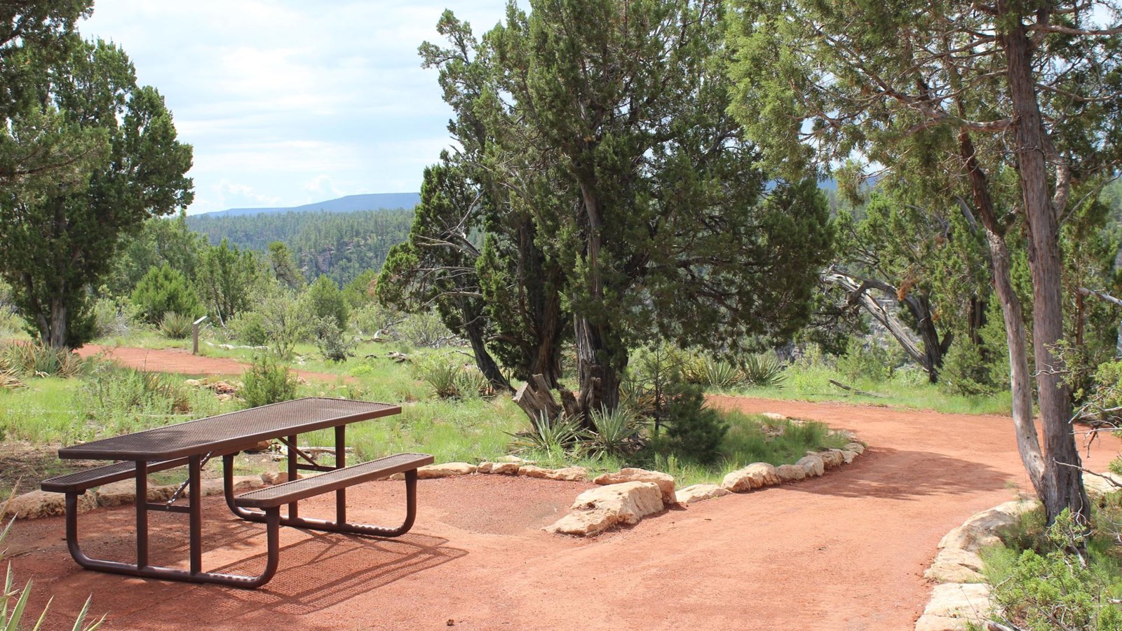 A brown picnic table is on the bottom left of the image. The Rim Trail is on the right.