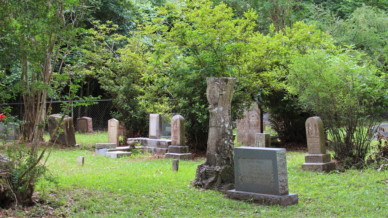 a cemetery with tall, prominent gravestones, in a grassy area surrounded by trees