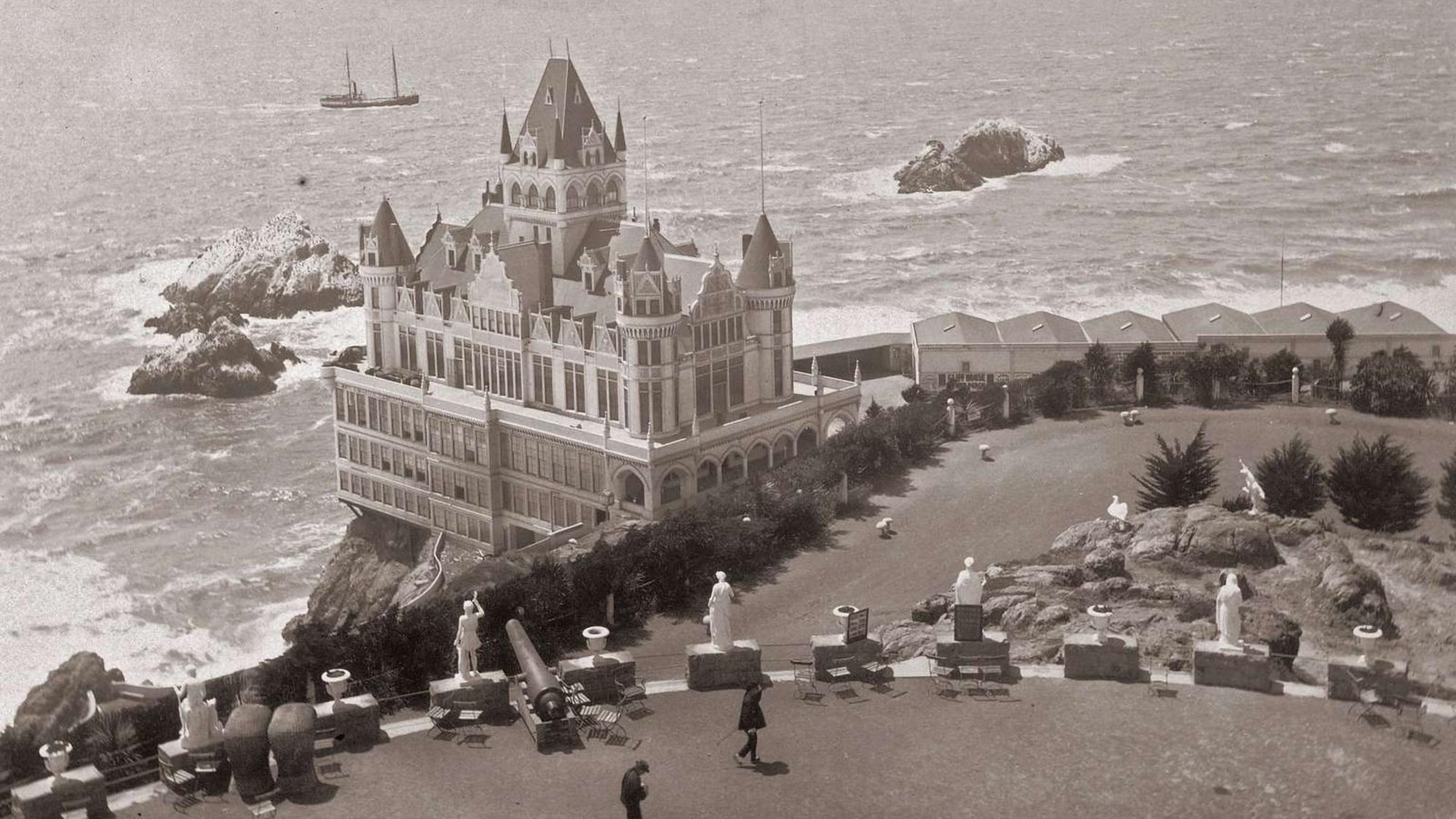 A view from Sutro\'s mansion looking down past cannons and statuary to Sutro\'s Cliff House