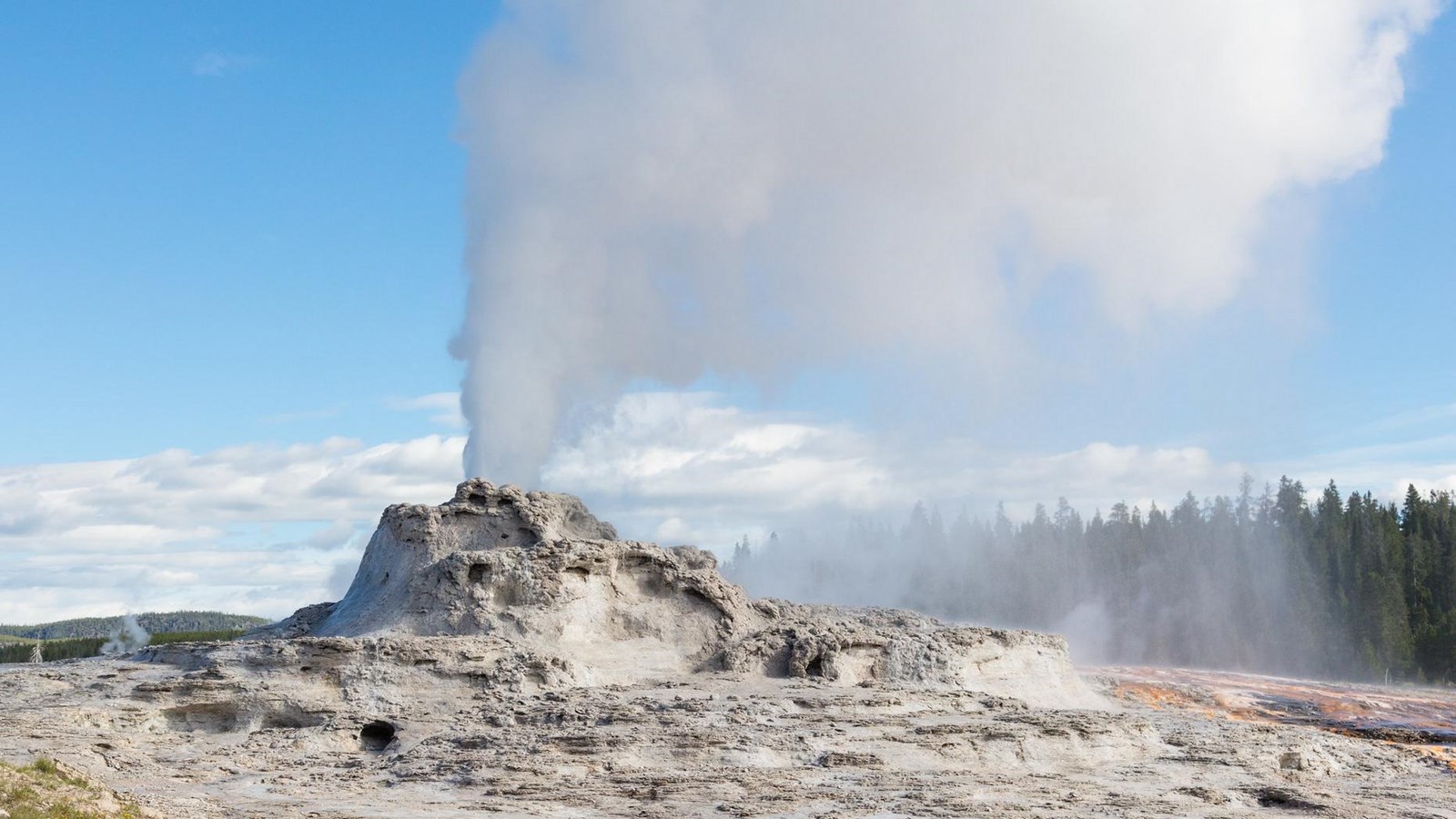 A large cone geyser with steam rising above against a blue sky