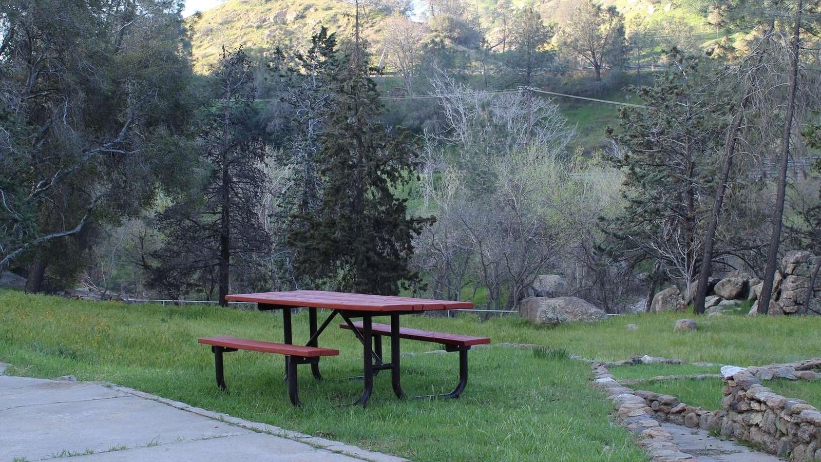 A picnic table surrounded by green grass and concrete and rock walkways