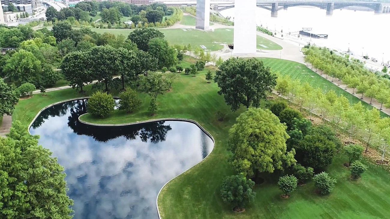 looking down at a pond with a curving edge reflecting clouds surrounded by green landscape