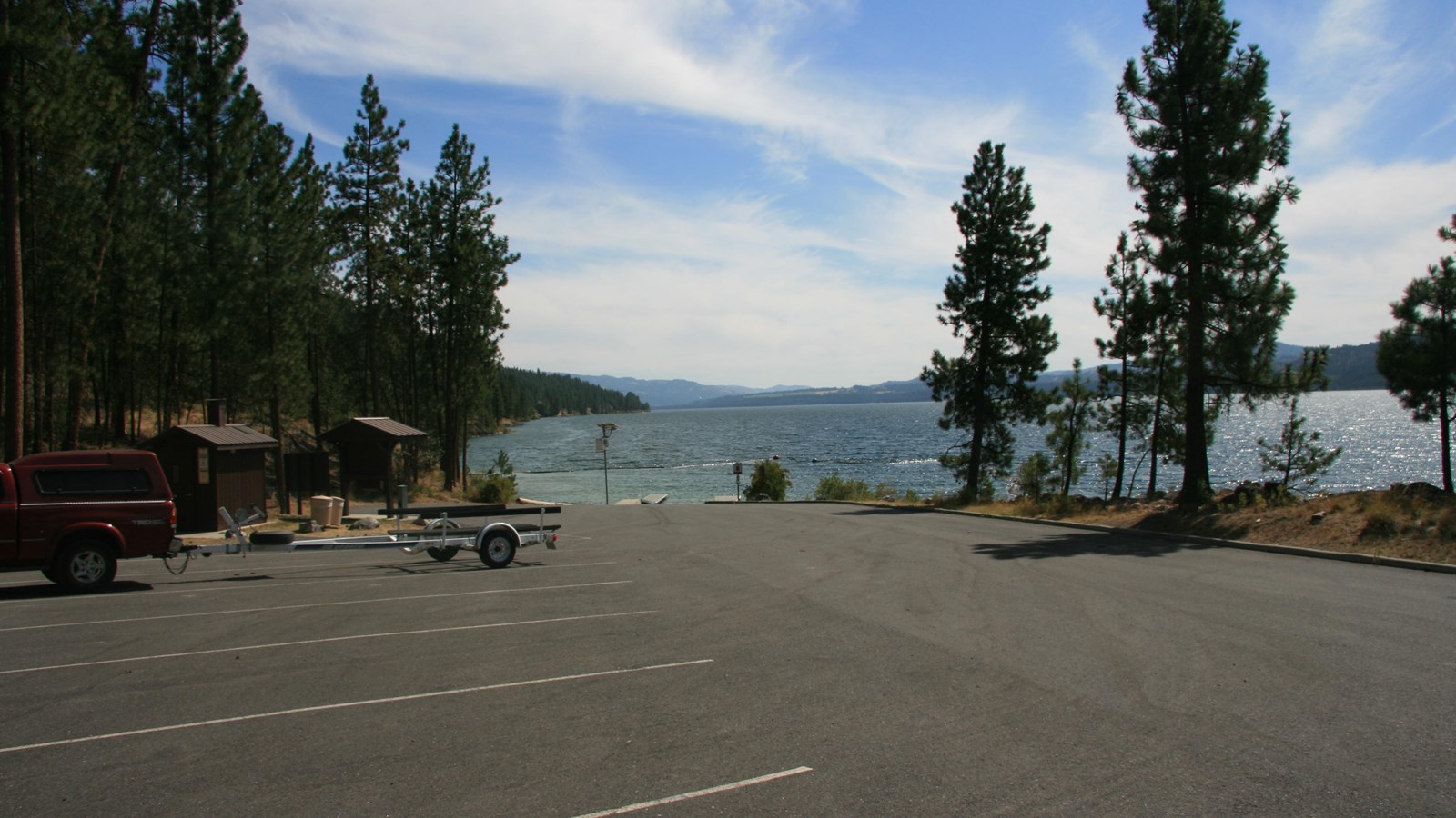 A view looking over the parking area toward the boat launch, trees to the left, and lake beyond.