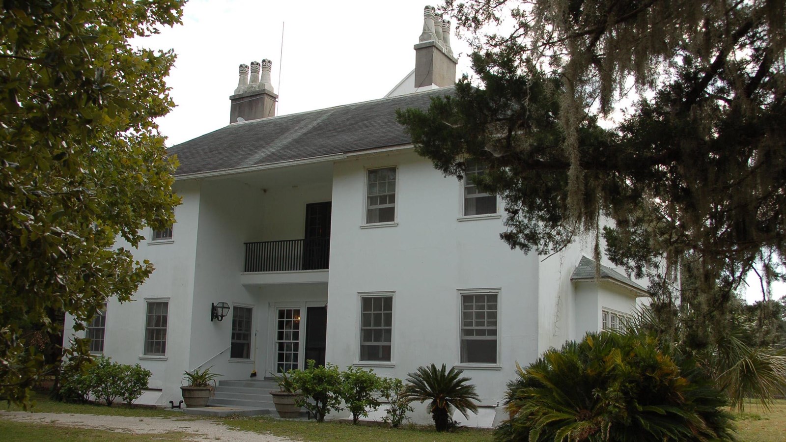 Two-story white house with sand path leading to and grass lawn with trees