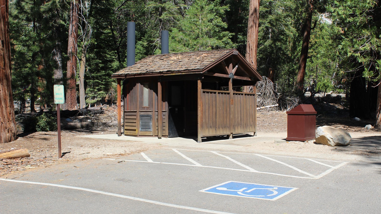 An brown, accessible vault toilet restroom is pictured with accessible van parking in foreground.