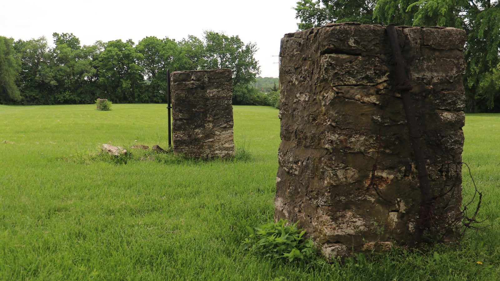 Two stone gate posts in the foreground, and pasture, trees, and stone gate posts in background