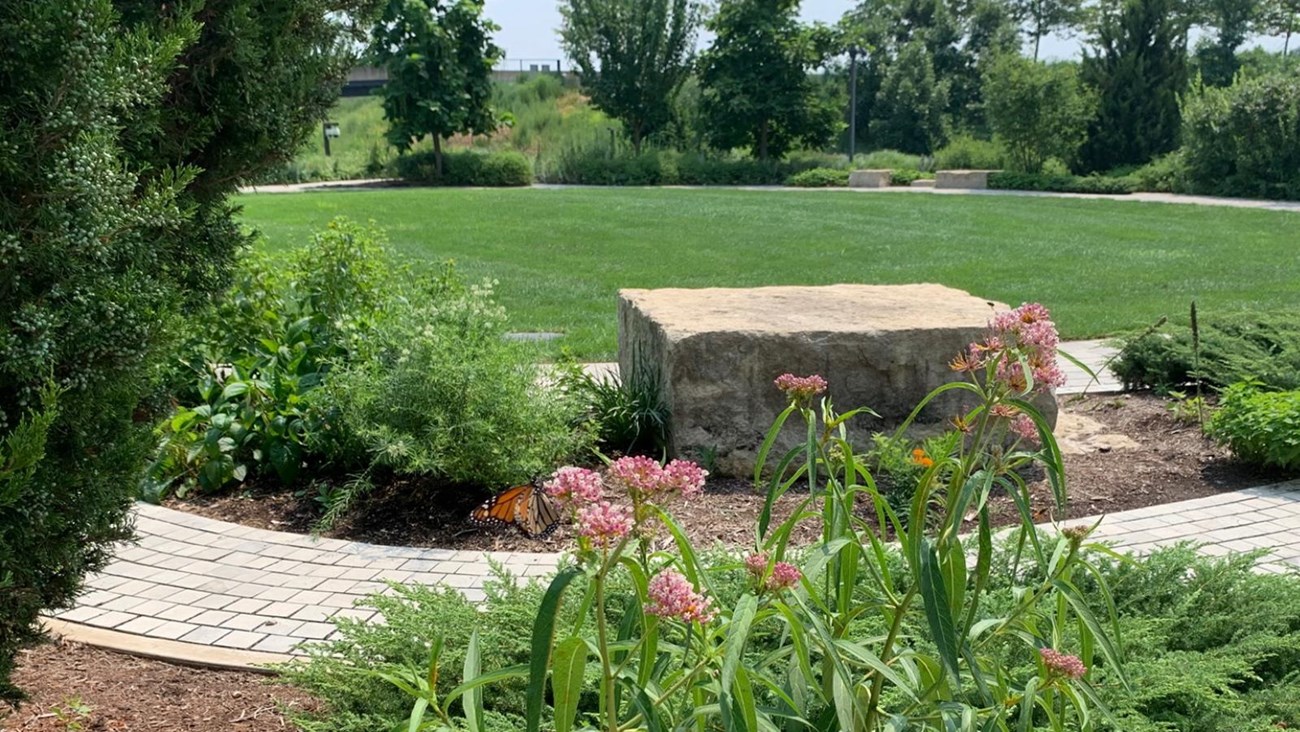 a stone block along a curved path in front of a green lawn with plants surrounding