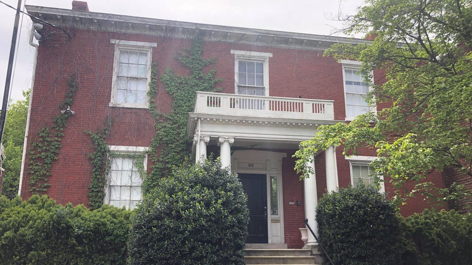 a two-story red brick building with hedges circling the building and vines crawling up the walls.
