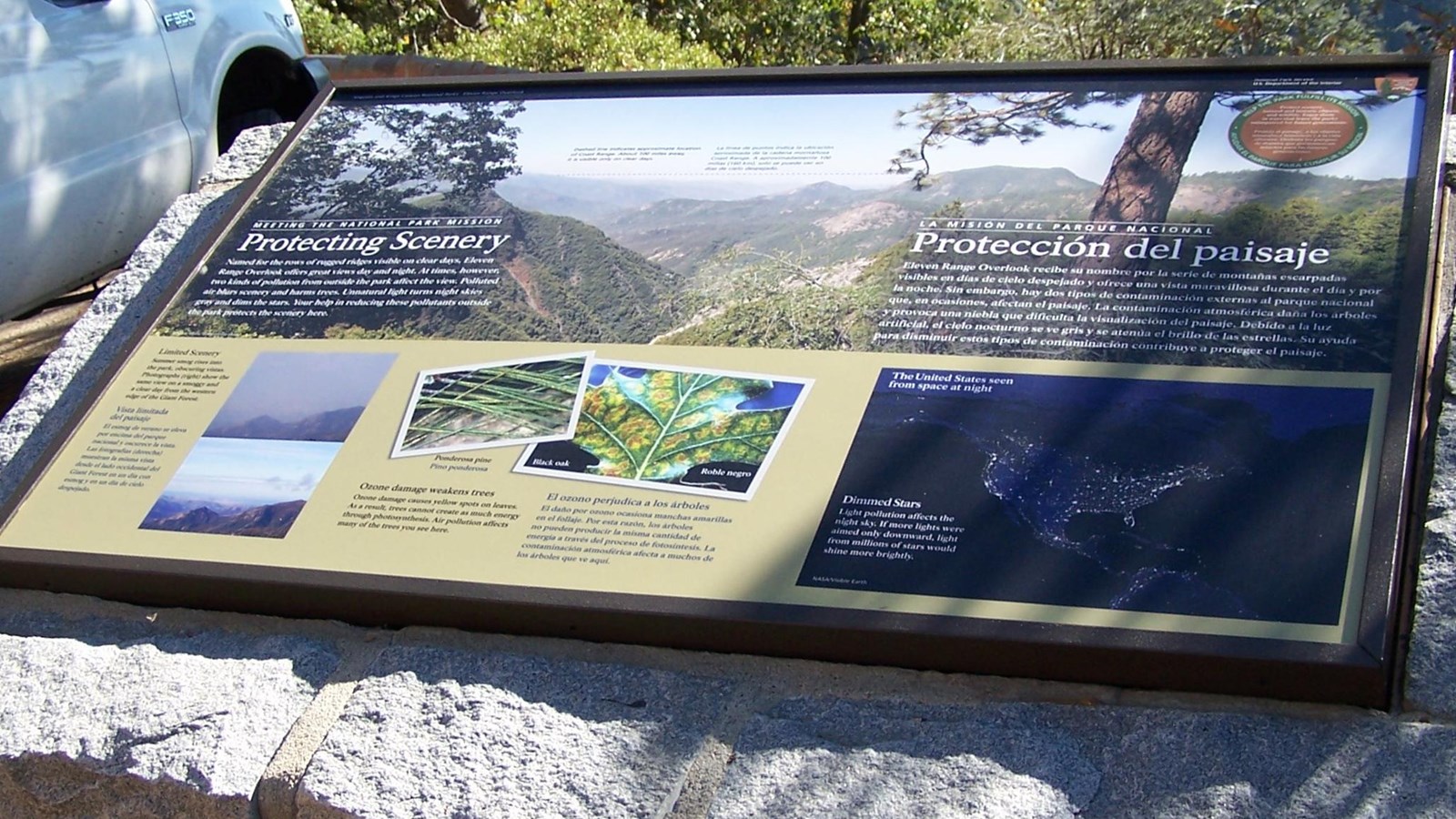 An exhibit sign mounted on a stone base discusses air pollution in the parks.