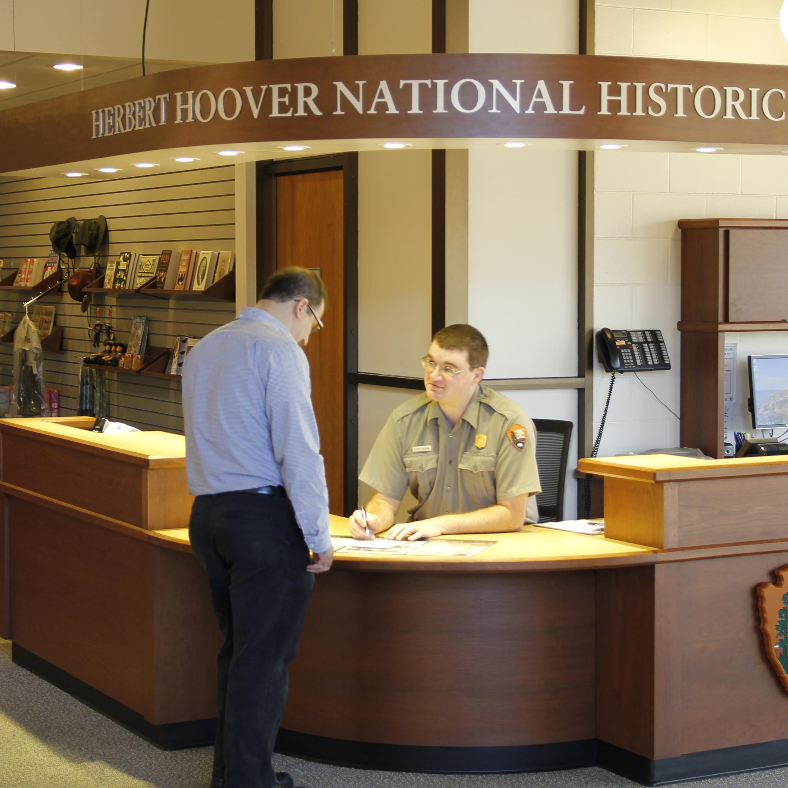 A uniformed ranger at an information desk assists a park visitor.