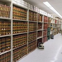 Tall bookcases line the length of the image, with white floors and flourescent lights