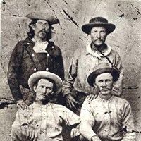 Historic image of four men sitting for a portrait wearing western American 1860s era clothing.