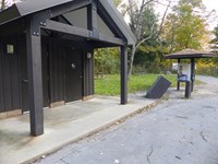 Two door restrooms (left) and a three sided information kiosk along the driveway with a trail (right