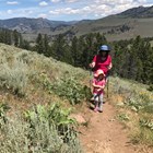 Mother and daughter hike up a trail with mountain scenery behind them.