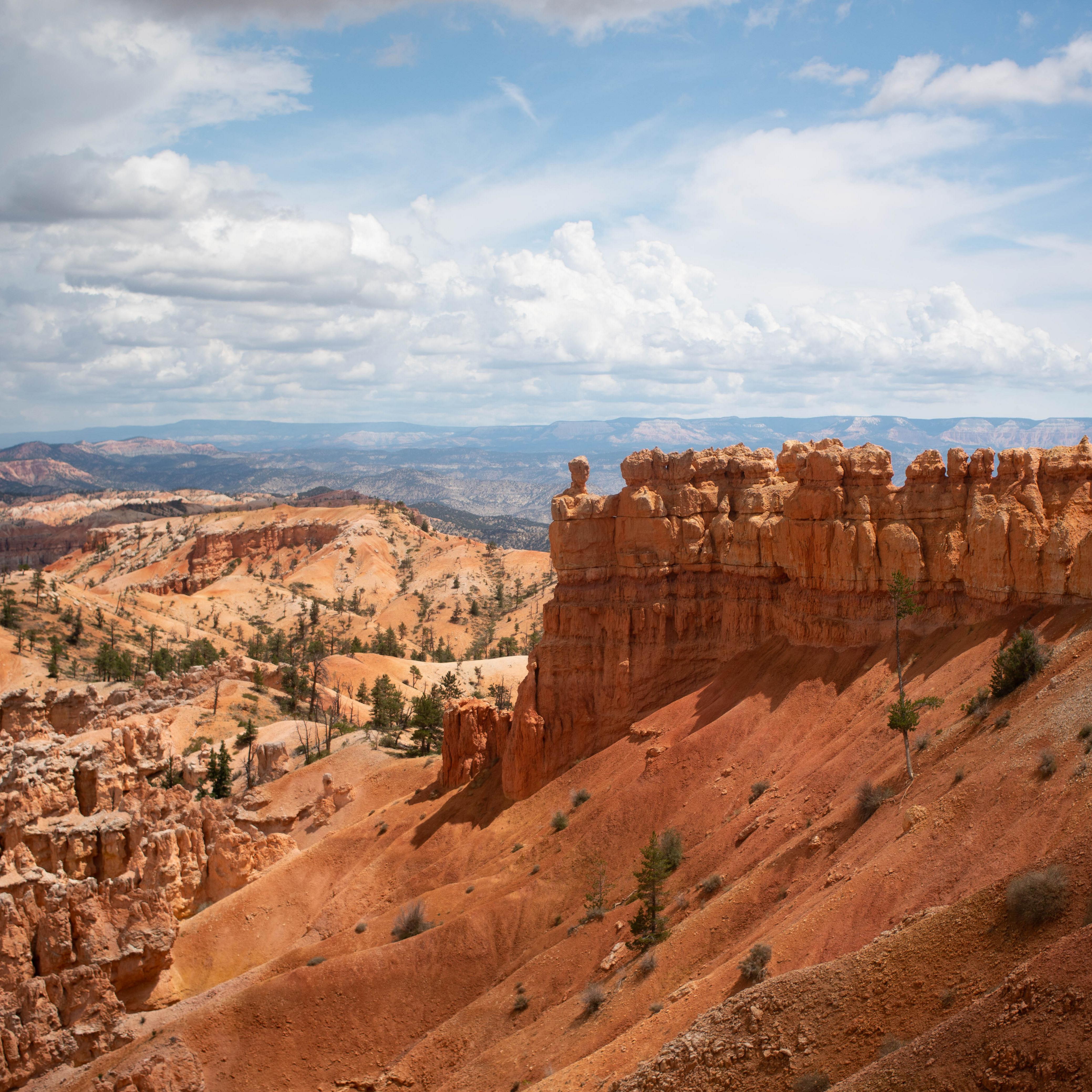 Red rock formations on top of a steep sandy slope with distant red rock formations in the background