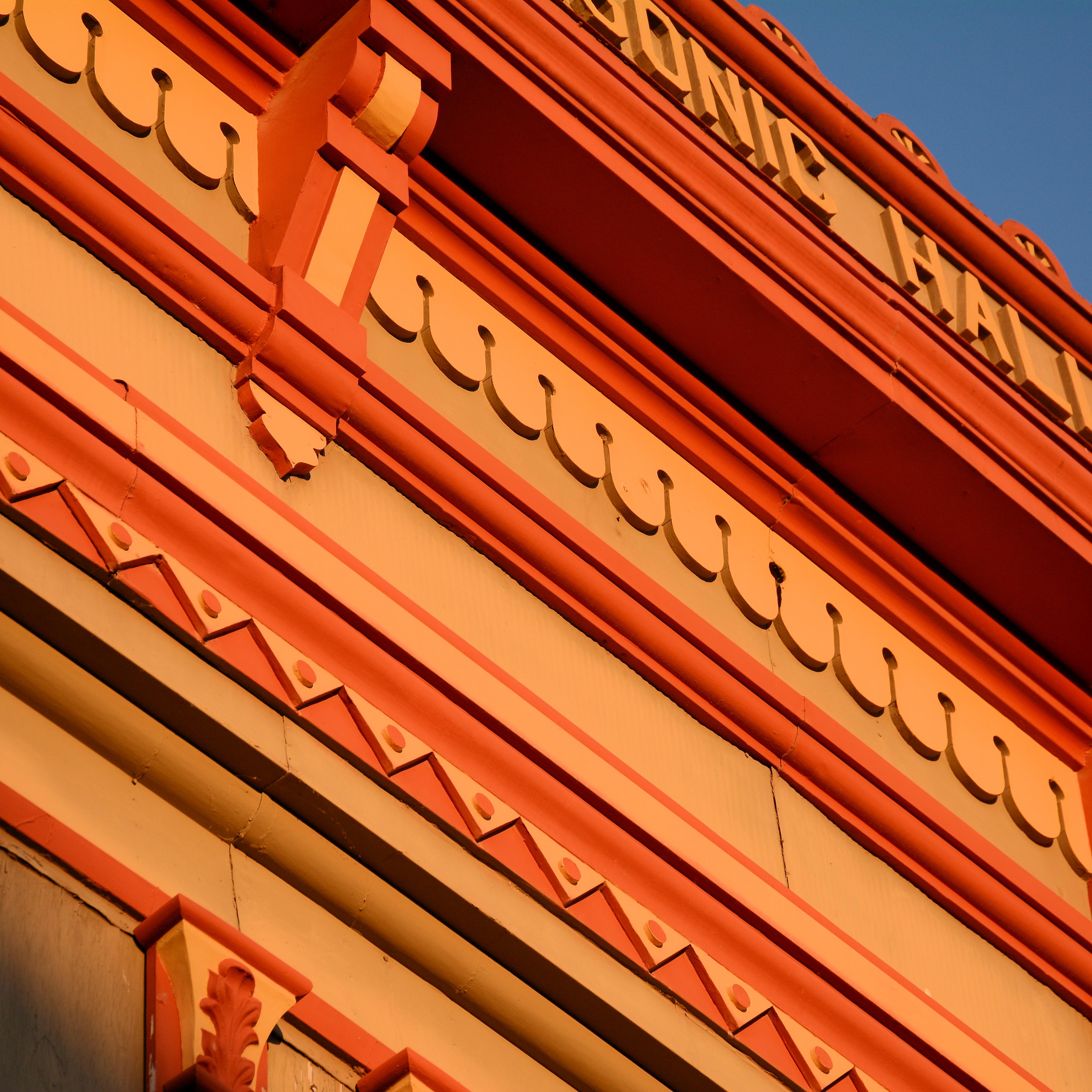 A detail photo of a building cornice shows courses of red and orange decorations.