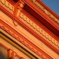 A detail photo of a building cornice shows courses of red and orange decorations.
