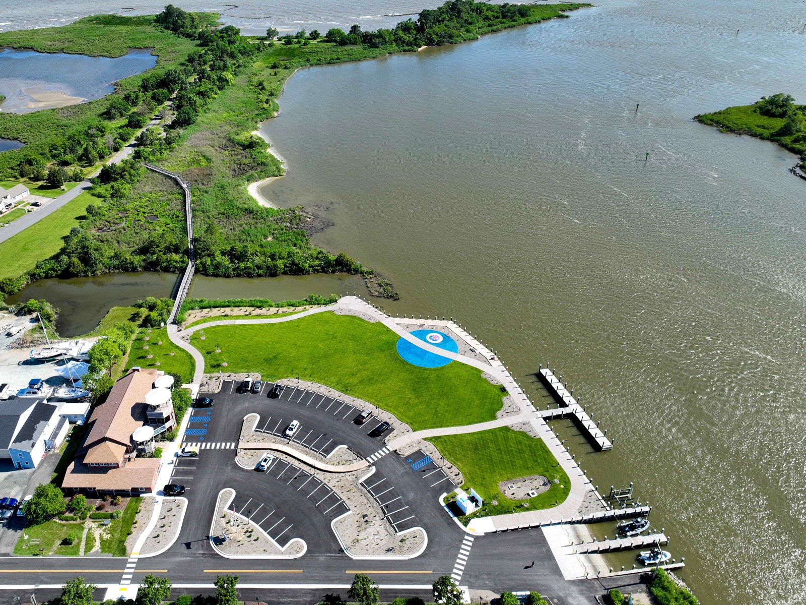 Aerial view showing a marina, buildings, parking lots, green spaces, and open water