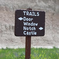 a brown sign with white writing points to door, window, notch, and castle trails.