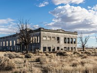Color photograph of a large block neoclassical building in ruins surrounded by a fence