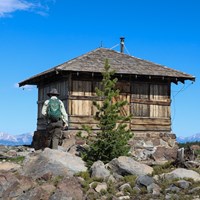 A hiker approaches a fire lookout on top of a mountain.