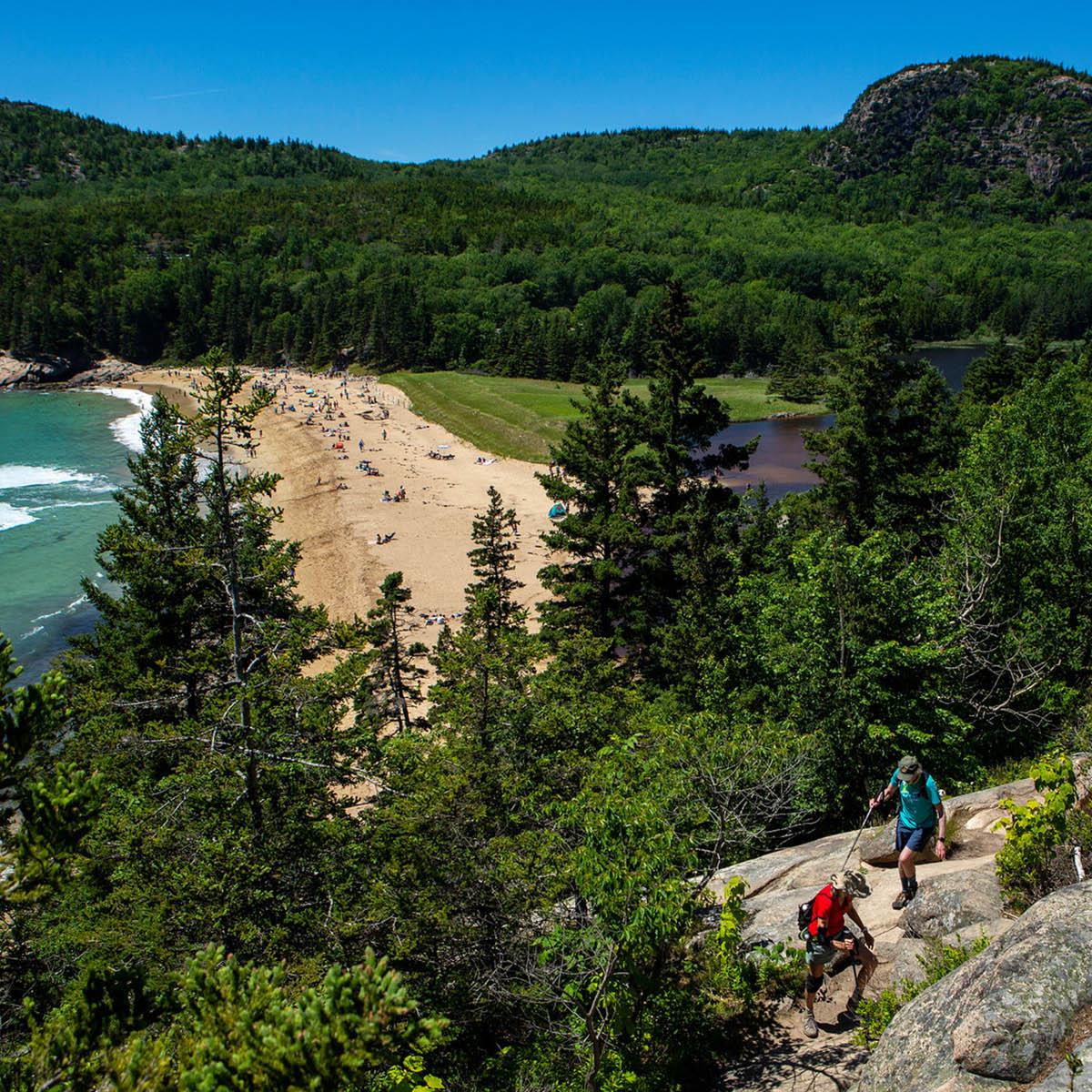 Two hikers walk along Great Head Trail overlooking Sand Beach.
