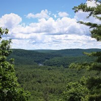 View overlooking lush river valley. Clear river cuts through rolling green tree-covered hills.