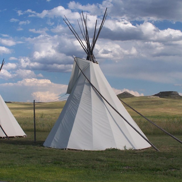 Two canvas covered tipis with the Agate Fossil Hills in the distance.