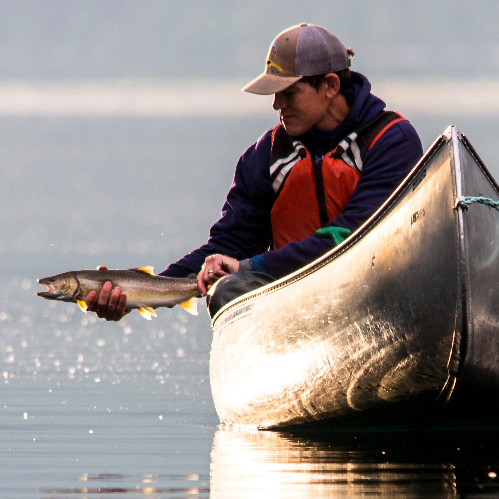 A man catches a fish while in a canoe.