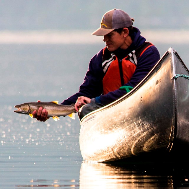 A man catches a fish while in a canoe.