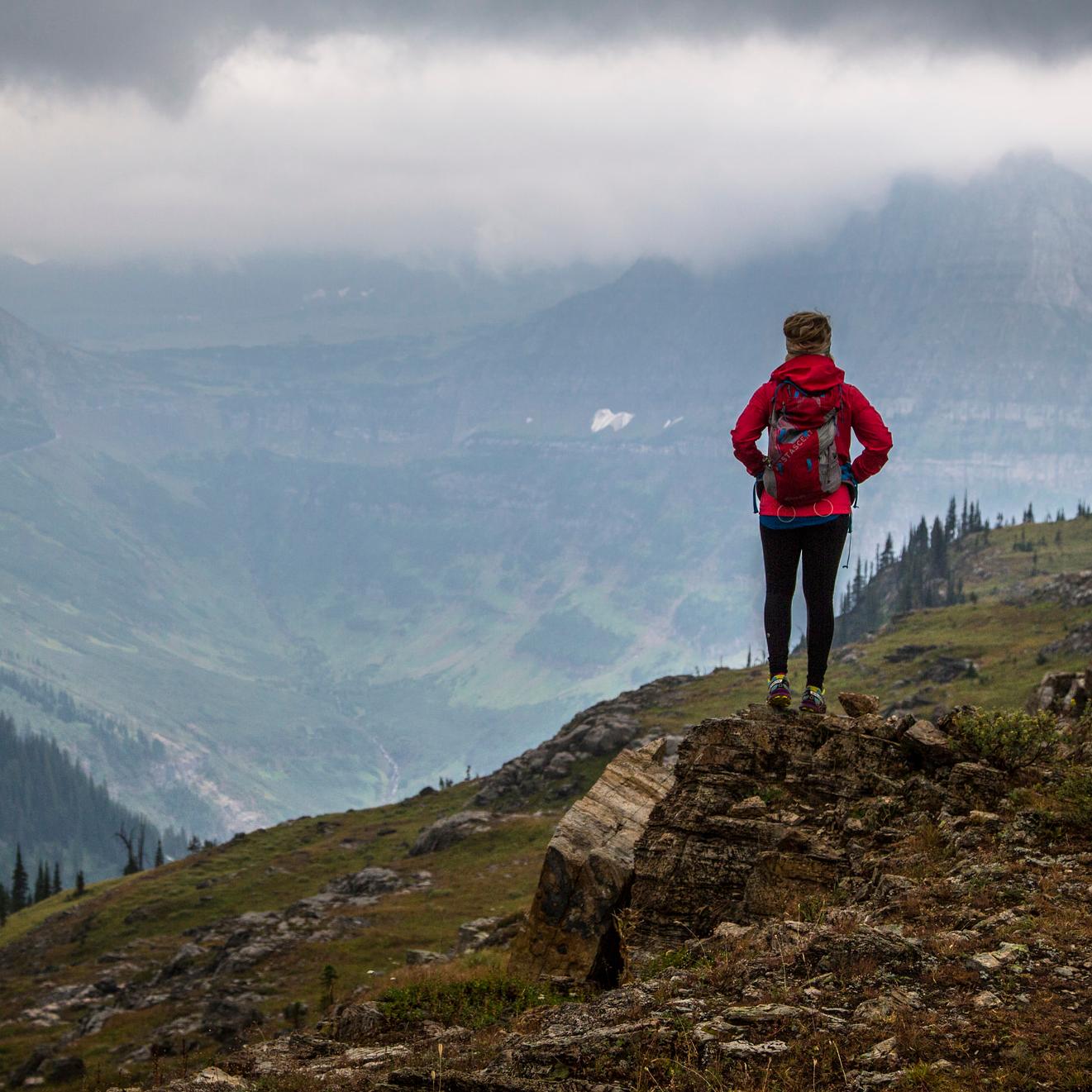 Woman standing on rock faces cloud filled mountain valley